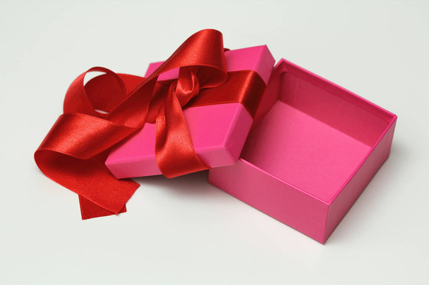 Pudełko zapakowane w ręcznie brązowy papier i wiązać różową satynową wstążkę. Białe tło. - Zdjęcie, obraz