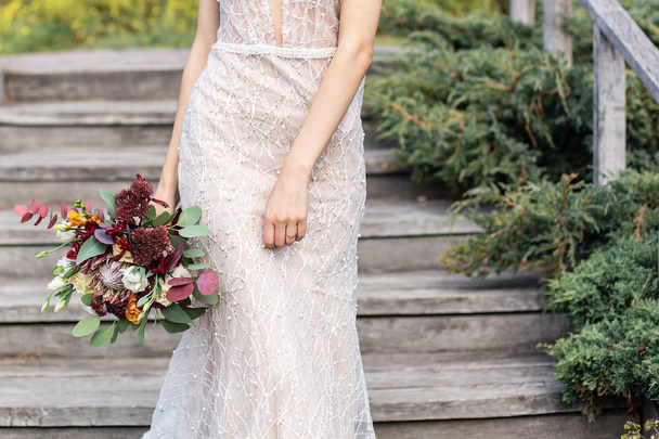 Handgemachtes Brautkleid auf der Braut, die einen schönen Strauß hält - Foto, Bild