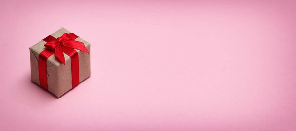 Gift box wrapped in brown craft paper and tie red satin ribbon. Pink solid background. Sale concept. Long horizontal banner photo format. Your text space. - Photo, image