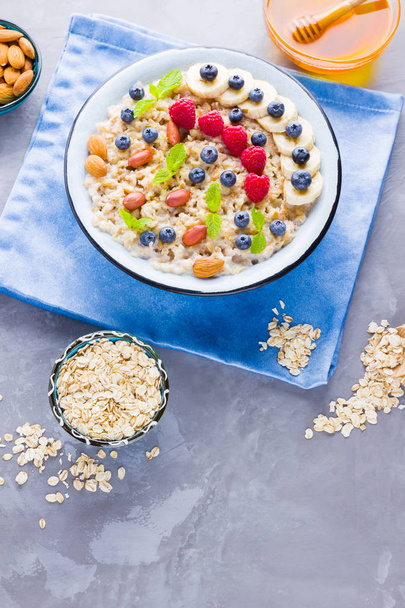 Healthy breakfast. Oatmeal porridge with berries, fruits and honey on cement background. Tasty oatmeal with raspberries, blueberries and nuts on blue napkin - Foto, Bild