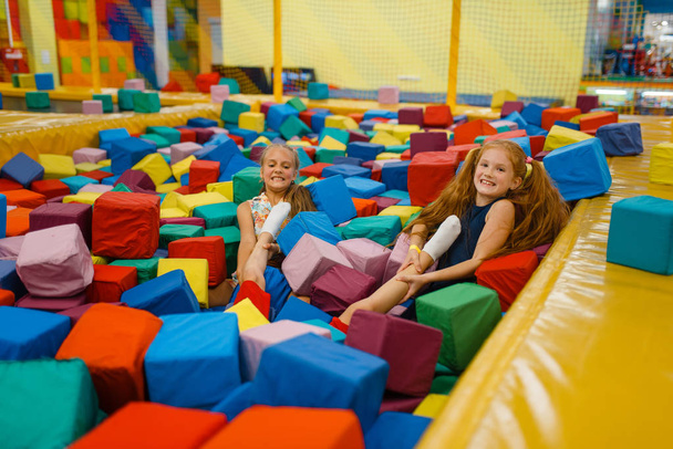zwei kleine Mädchen liegen in weichen Würfeln, Spielplatz im Unterhaltungszentrum. Spielbereich drinnen, Spielzimmer - Foto, Bild