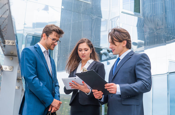 Confident businesspersons talking in front of modern office building. Businessmen and businesswoman have business conversation. Banking, professional job and financial market concept. - Fotoğraf, Görsel