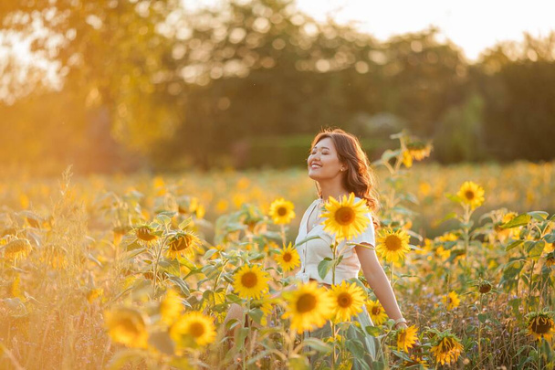 Mulher asiática jovem com cabelo encaracolado em um campo de girassóis ao pôr do sol. Retrato de uma jovem bela mulher asiática ao sol
. - Foto, Imagem