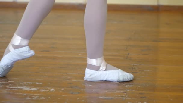 Крупным планом девушки в белых балетных туфлях на старом деревянном полу во время балетной подготовки. Элемент упражнений классического танца
. - Кадры, видео