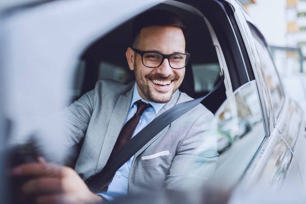 Cheerful caucasian businessman driving himself to work. Hands are on steering wheel. - Zdjęcie, obraz