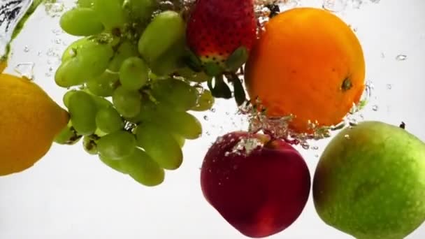 Appel, kiwi, sinaasappel, peer, citroen, druif en aardbei vallen in het water met bubbels. Videografie in slow motion - Video