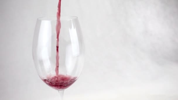 Şarap beyaz arka planda şeffaf büyük bir bardağa dökülüyor. - Video, Çekim