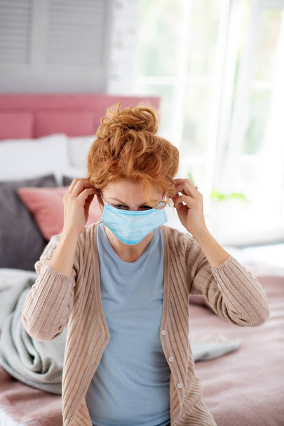 Woman wearing beige cardigan putting protective mask on - 写真・画像