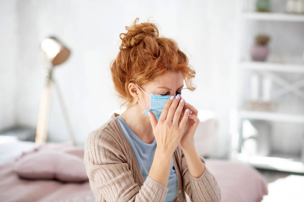 Curly woman sneezing after putting protective mask on - Foto, imagen