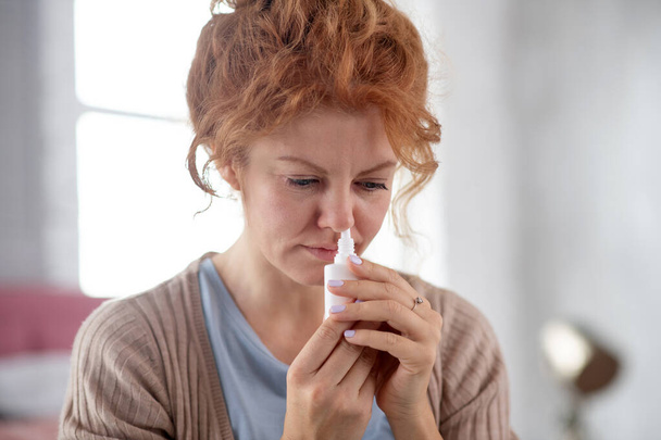 Femme aux cheveux roux utilisant un spray nasal alors qu'elle souffre de froid
 - Photo, image