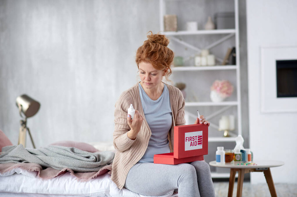Red-haired woman taking nasal spray out of first aid kit - Photo, Image