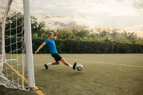 Erkek futbolcu topa vurur ve kapıyı kurtarır. Açık stadyumdaki futbolcu, maçtan önce antrenman, futbol antrenmanı. - Fotoğraf, Görsel