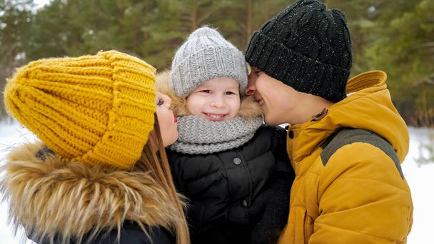 Mom and dad are cuddling and kissing their little son in winter park. - Fotografie, Obrázek