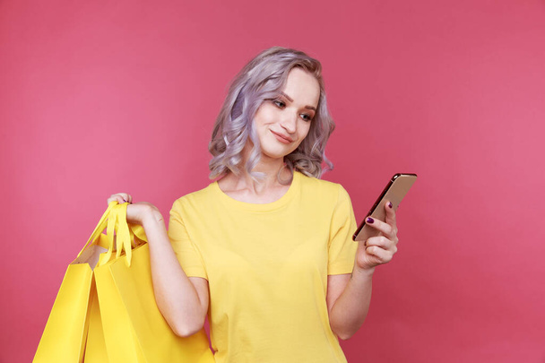 Online shopping concept. Cute young woman watching her phone and holding bags isolated. - Fotoğraf, Görsel