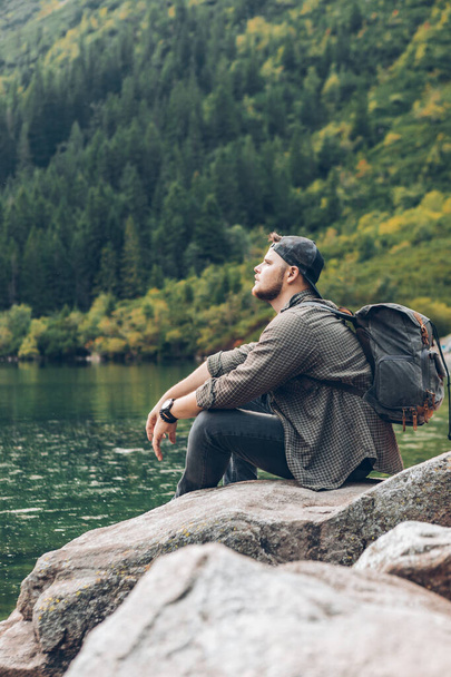 homme assis sur le rocher en face du lac dans les montagnes profitant de la vue
 - Photo, image