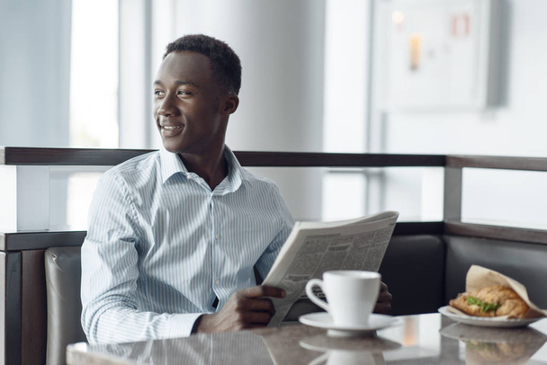 Молодой африканский бизнесмен с газетой обедает в офисном кафе
. - Фото, изображение