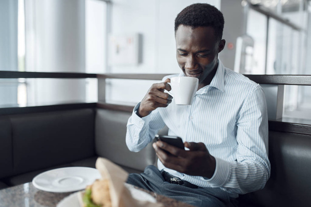 Young African businessman with newspaper having lunch in office cafe. - Valokuva, kuva