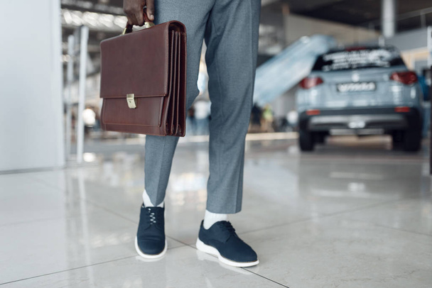 Businessman holds briefcase in car showroom. - Photo, Image