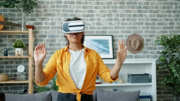 Young African American lady enjoying vr glasses in apartment moving hands - Video