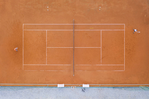 horní pohled na oranžové hliněné hřiště, kde dva hráči hrají sportovní tenisový zápas - Fotografie, Obrázek