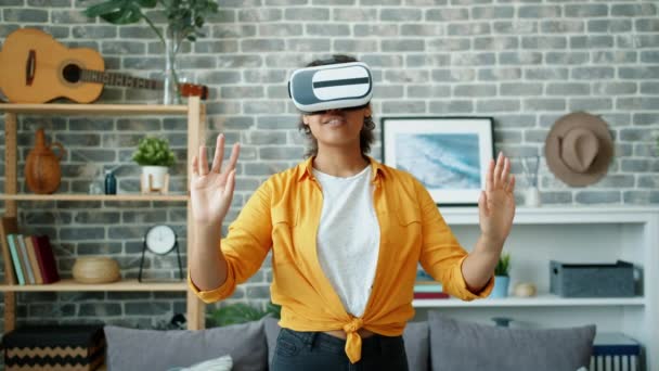 African American woman in virtual reality glasses moving arms smiling at home - 映像、動画