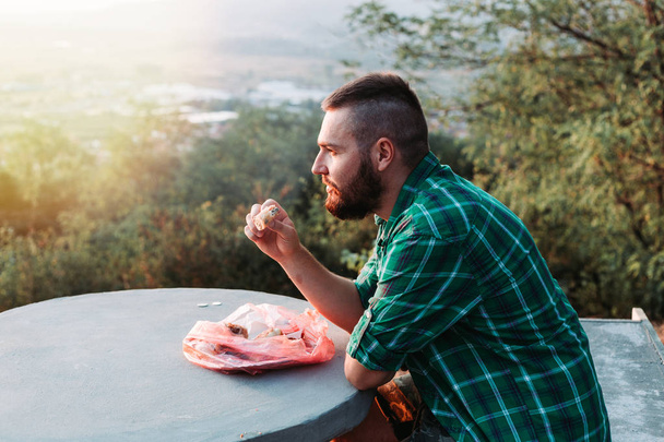 Bearded guy eating some pie, resting on the bench enjoying the view. - Zdjęcie, obraz