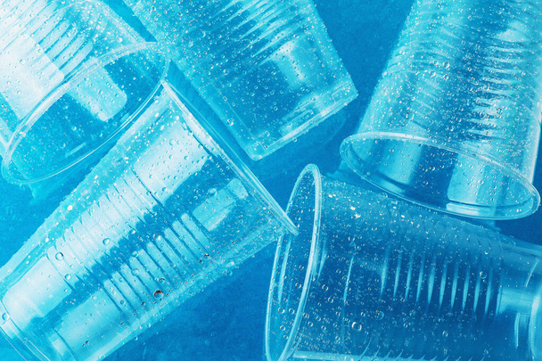 leere transparente Einweggläser aus Kunststoff in Wassertropfen auf hellblauem Hintergrund, Ansicht von oben - Foto, Bild