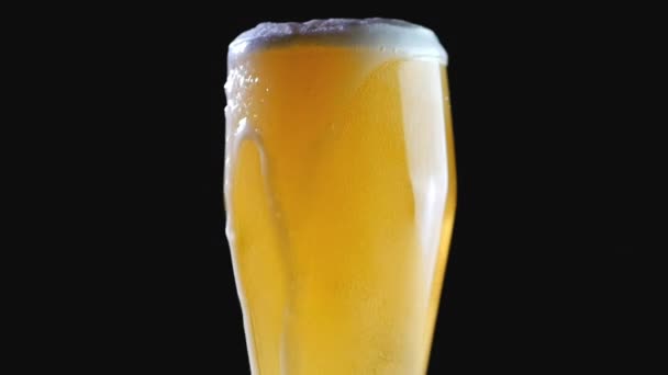 Beer is poured into the glass on a black background. Foam quickly slides through the glass. Extreme large beer foam and bubbles. - Video