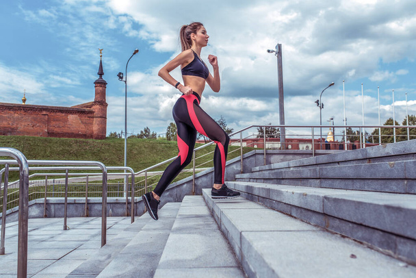 Sports girl runs in summer in the city. Sportswear Leggings Top. Cloud stair background. Motivation for fitness and workout lifestyle. Free space for text. - Fotoğraf, Görsel
