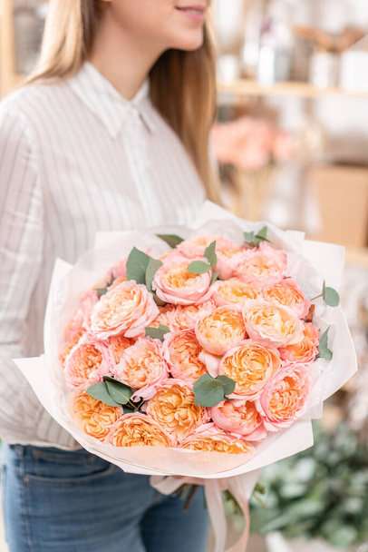 Багато бутонів троянд різнокольорового, пастельно-рожевого і блідо-оранжевого кольору. Букет в руці жінки. роботи флориста в квітковому магазині концепція квіткового магазину
 - Фото, зображення