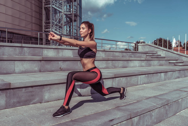 Girl athlete in summer in city does stretching and gymnastics. Workout before morning jogging, fitness outdoor workout. Tanned and slim figure, motivation for woman lifestyle. - Φωτογραφία, εικόνα