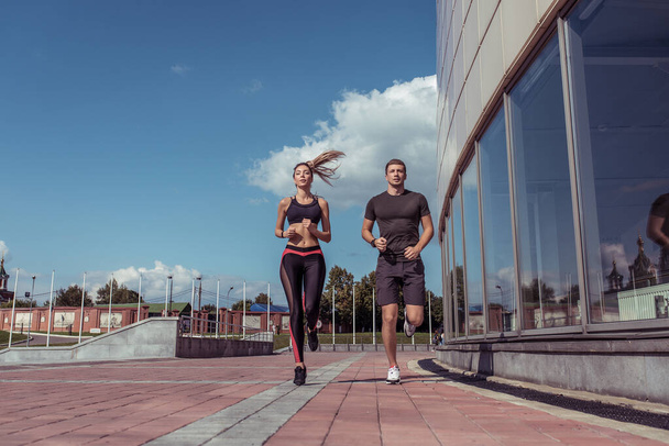 Athletic couple man woman, summer in city, jogging in jump, free space for text motivation fitness and workout, sportswear. Background tile and glass windows. - Fotó, kép