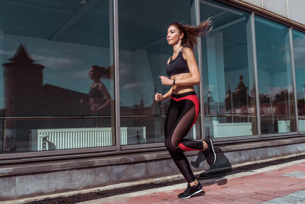 Sport woman run summer city. Sportswear Leggings Top. Background showcase glass windows. Motivation fitness workout lifestyle. Free space text. Tanned slender figure jump strong bold confident girl . - 写真・画像