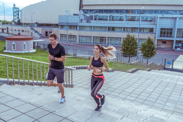 Athletic couple man and beautiful woman, in summer in city, run jogging on stairs, free space for text motivation fitness and workout, sportswear. - Foto, immagini