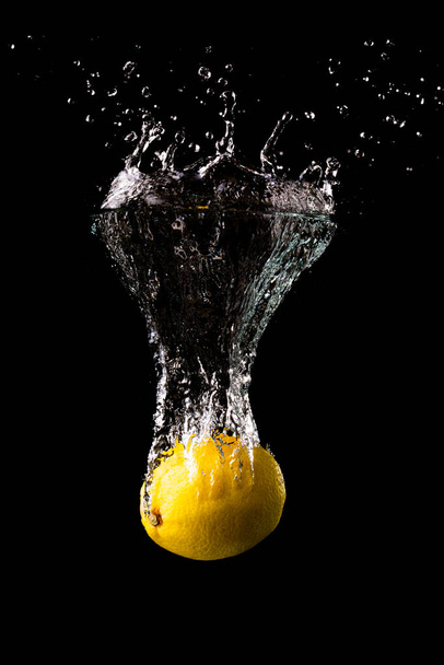 Свіжий жовтий лимон у воді бризкає на чорному тлі з великою кількістю
 - Фото, зображення