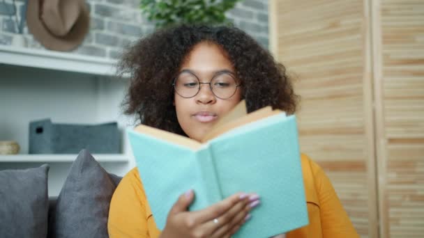 Pretty African American woman reading book at home turning pages smiling - Footage, Video