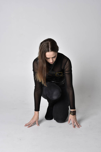 full length portrait of a pretty brunette woman wearing black leather fantasy costume. Crouching pose on a studio background. - Fotó, kép