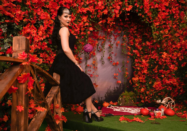 Тонка дівчина моди Хеллоуїн з чорним волоссям в мереживній готичній сукні, що позує на осінньому фоні з осіннім листям
 - Фото, зображення