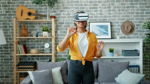 Happy Afro-American girl playing game in virtual reality glasses in apartment - 映像、動画
