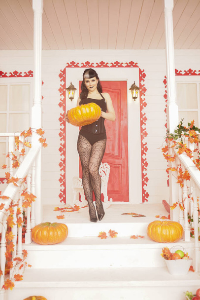 Mujer sexy caliente vienen para truco o tratar la noche de Halloween. Chica vampiro gótico en el porche blanco de la casa de otoño decorada
. - Foto, imagen