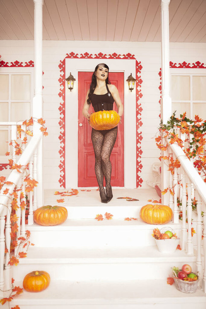 Hete sexy vrouw komt voor truc of trakteer Halloween avond. Gothic vampier meisje op witte veranda van versierde herfst huis. - Foto, afbeelding