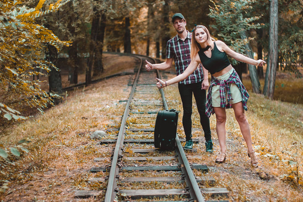 Egy fiatal szerelmespár lekéste a vonatot. Stopposok a síneken az őszi erdőben várják a következő vonatot.. - Fotó, kép