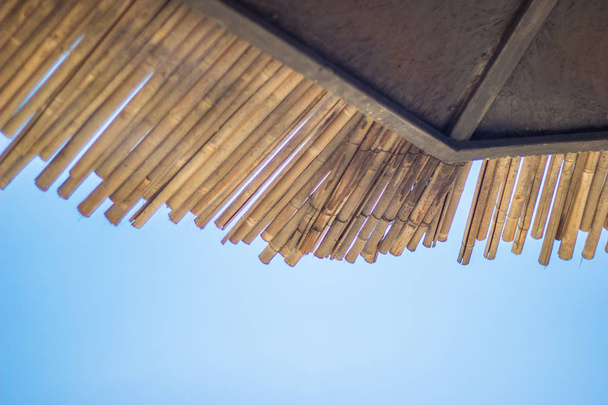 Wicker roof beach umbrella and blue sky. Natural bamboo sunshades and summer umbrella parasol on blue sea shore. Large straw beach umbrellas. - Photo, Image