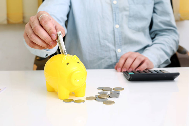  Bild einer Person, die Geld in einem gelben Sparschwein deponiert. isoliert im Hintergrund. - Foto, Bild