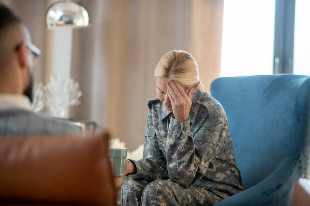 Blonde military woman having headache while remembering stressful events - Фото, изображение