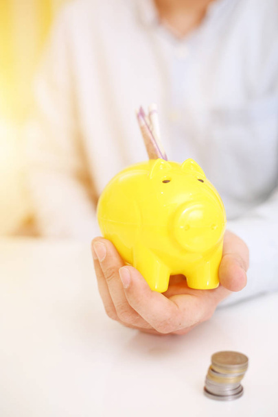  Bild einer Person, die Geld in einem gelben Sparschwein deponiert. isoliert im Hintergrund. - Foto, Bild