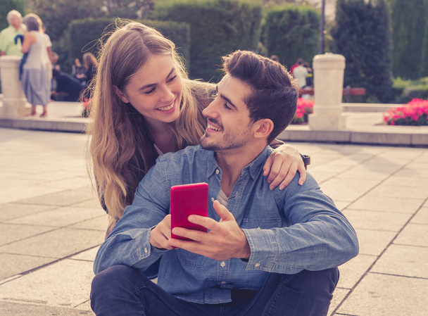 Young couple on social media using smart phone app to post and comment in blog online. Young man and woman looking online inluencers and sharing photos in social network with family and friends. - Φωτογραφία, εικόνα