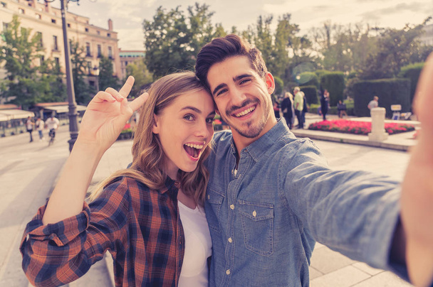 Beautiful friends tourist couple in love taking selfies at sunset while walking and visiting an European city outdoors in a romantic vacation. In Tourism, travel destination and vacation concept. - Photo, Image