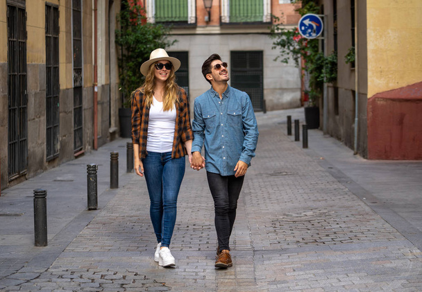 Young couple in love walking on street holding hands having fun traveling around Europe on vacation in a romantic trip or city break. In tourism, lifestyle and travel concept. - Foto, imagen