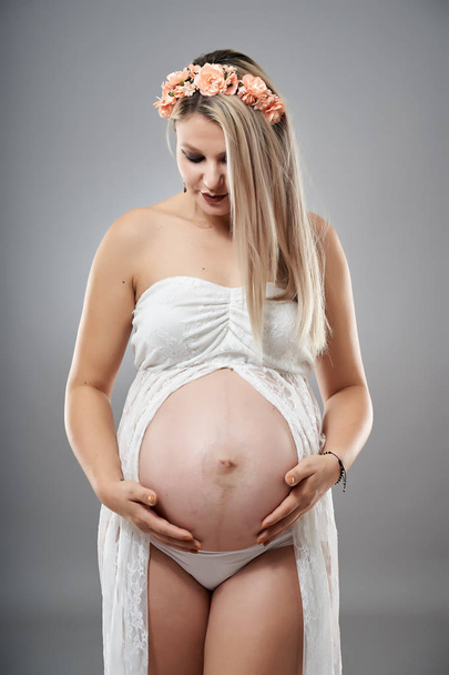 Studio portrait of a beauty pregnant woman in white clothes posing beside grey studio background  - Φωτογραφία, εικόνα